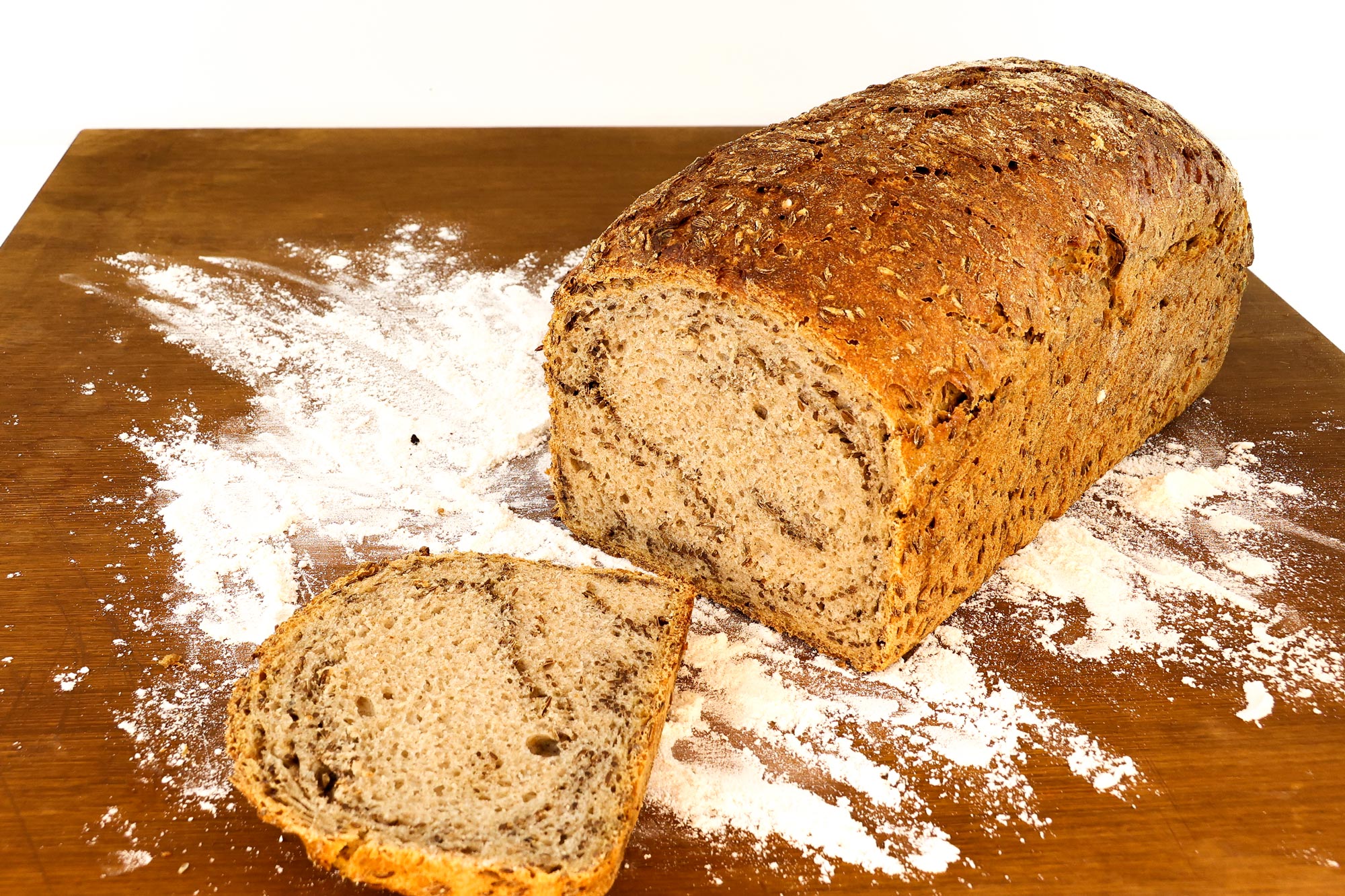 Angeschnittenes Kümmelbrot der Bäckerei Krämer mit goldbrauner Kruste auf bemehltem Holzbrett