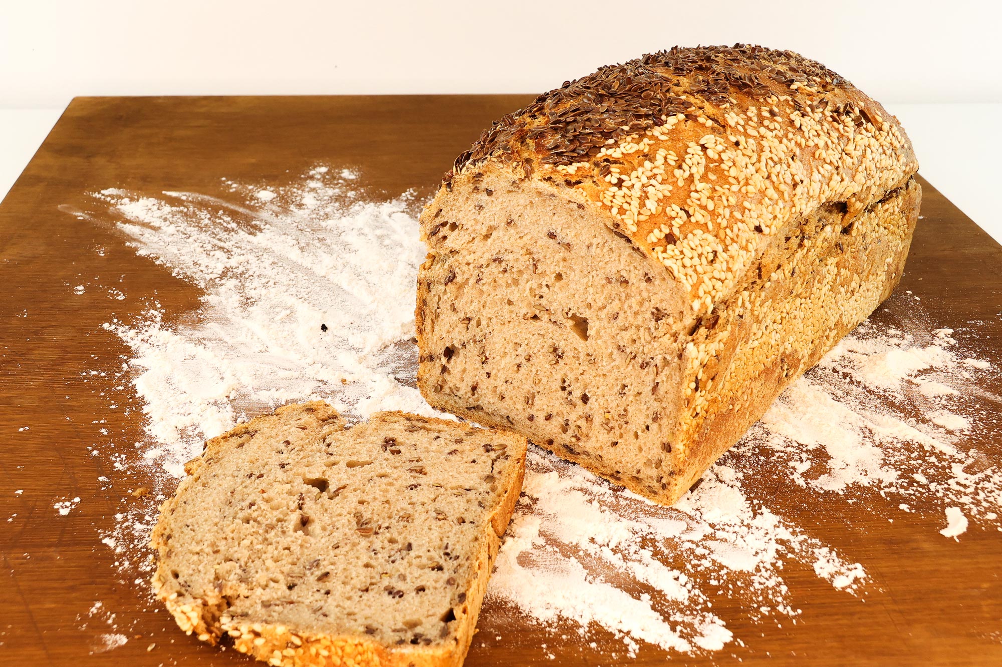 Angeschnittenes Leinsamen-Sesam-Brot der Bäckerei Krämer mit Sesam- und Leinsamenkruste auf bemehltem Holzbrett