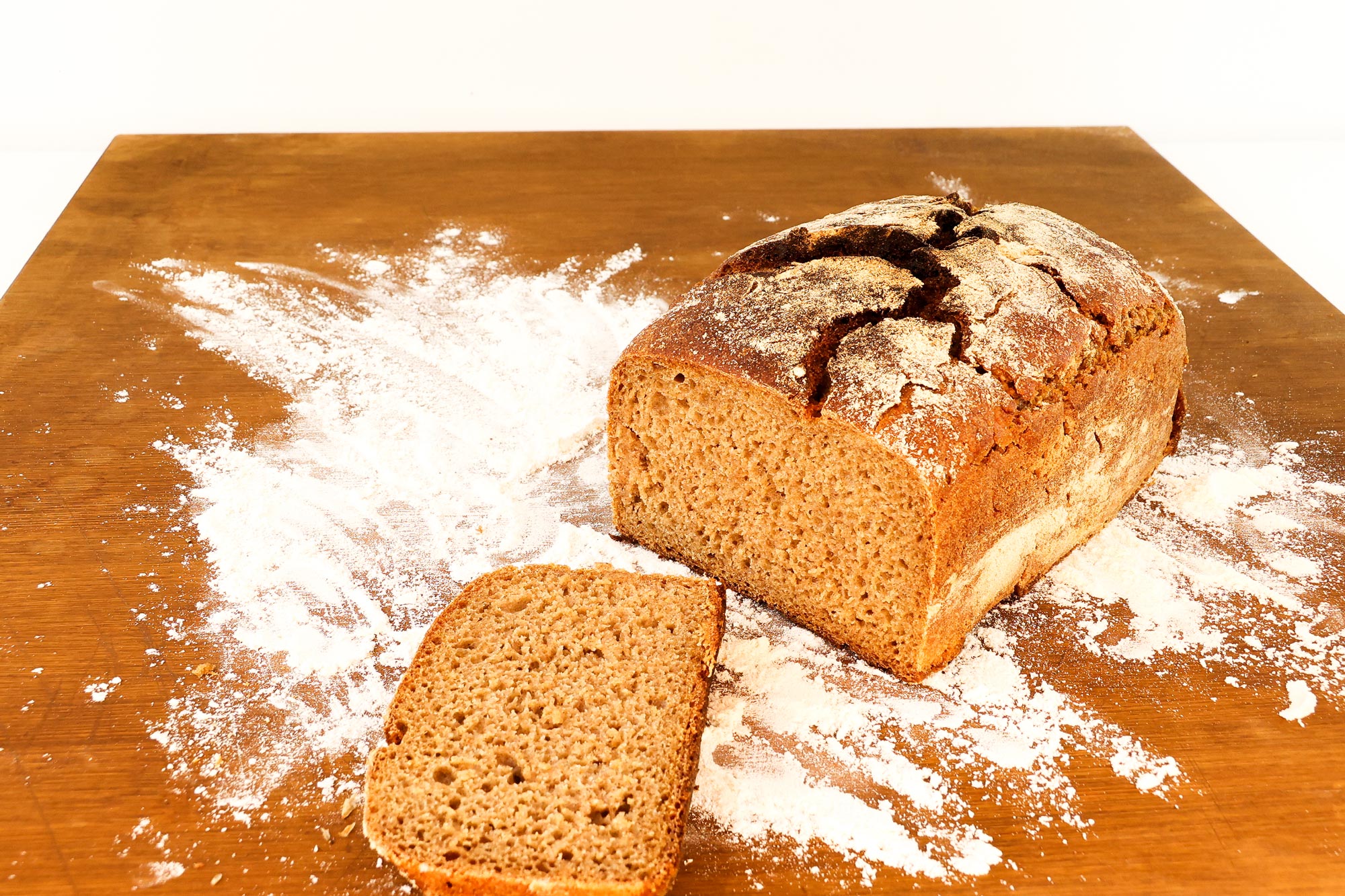 Angeschnittenes Schwarzbrot der Bäckerei Krämer mit bemehlter, aufgerissener Kruste auf bemehltem Holzbrett